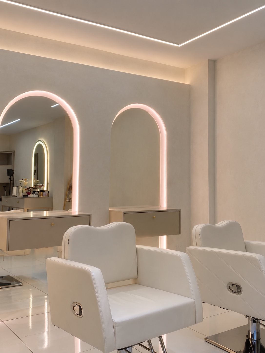 Bancadas de maquiagem com espelhos arqueados iluminados e poltronas claras no studio